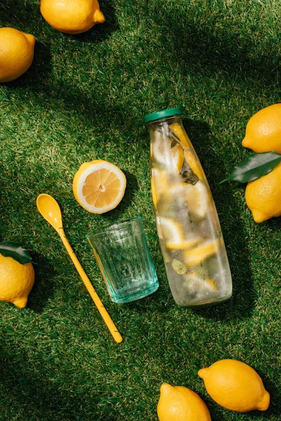 Vista superior de vidrio, cuchara, limones y botella de limonada en el césped verde - foto de stock