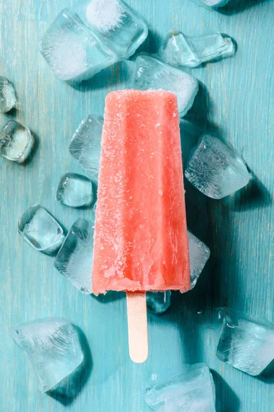 Червоний фруктовий лід поп на дерев'яному фоні з кубиками льоду — стокове фото