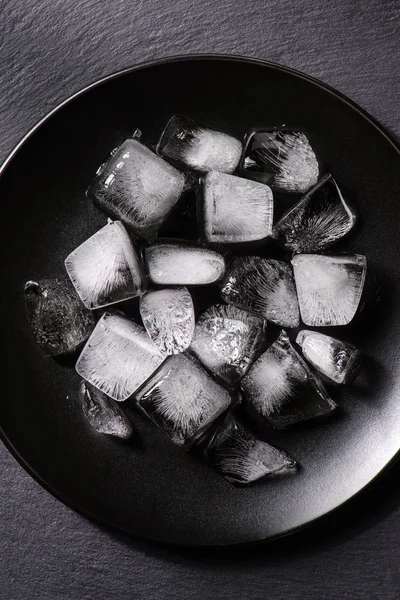 Cubos de hielo que se funden en placa negra sobre fondo oscuro - foto de stock