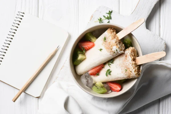 Deliciosos estallidos de hielo con bloc de notas en blanco sobre fondo de madera - foto de stock