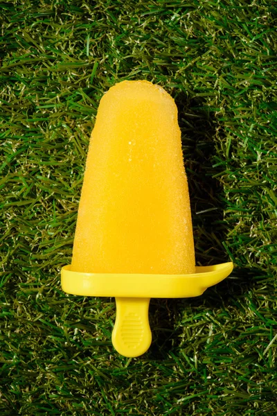 Pop de hielo amarillo sobre fondo de hierba verde - foto de stock