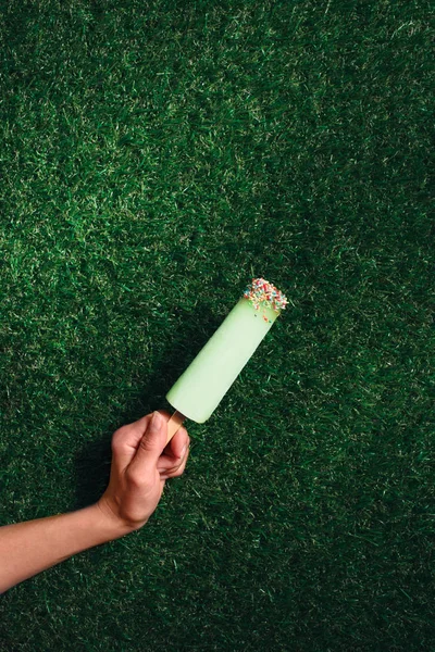 Delicious popsicle in hand on green grass background — Stock Photo