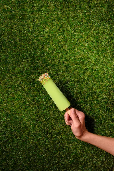 Main tenant de la glace aux fruits sur fond d'herbe verte — Photo de stock