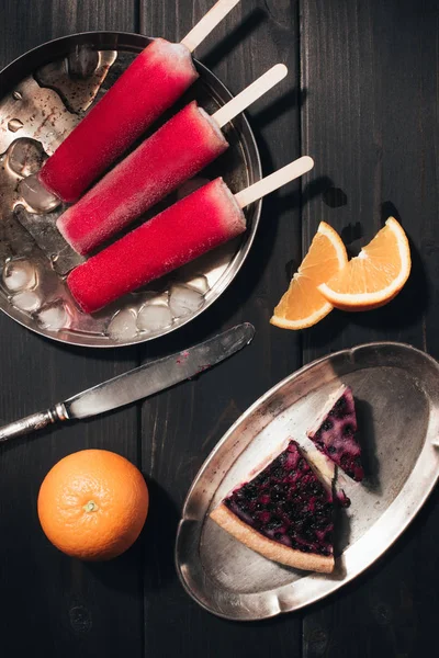 Paletas de frutas dulces con naranjas y pastel de bayas sobre fondo de madera - foto de stock