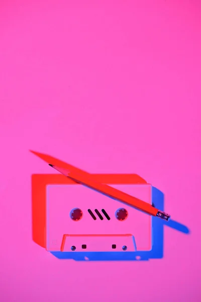 Toned pink picture of retro audio cassette and pencil on tabletop — Stock Photo