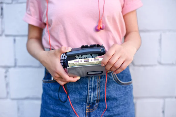 Cropped shot of woman with earphones holding retro cassette player in hands against white brick wall — Stock Photo