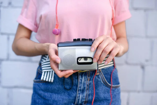 Cropped shot of woman with earphones holding retro cassette player in hands against white brick wall — Stock Photo