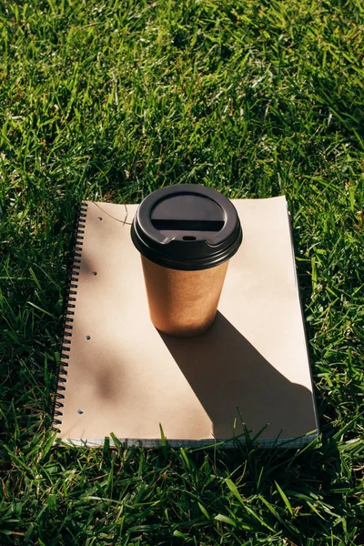 Close up view of coffee to go and notebook on green grass — Stock Photo