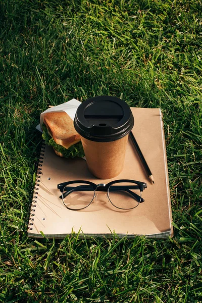 Vista da vicino di notebook, panino, occhiali e caffè per andare su erba verde — Foto stock