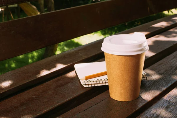 Vista da vicino del taccuino con matita e tazza di caffè usa e getta su una panca di legno — Foto stock