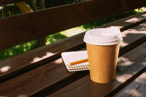 Cerrar vista de cuaderno con lápiz y taza de café desechable en banco de madera - foto de stock