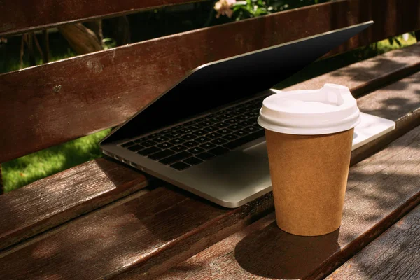 Vue rapprochée de l'ordinateur portable et du café pour aller sur un banc en bois — Stock Photo