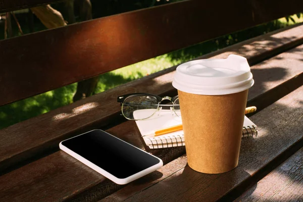 Vista de cerca de teléfono inteligente, portátil, anteojos y café para ir en banco de madera - foto de stock