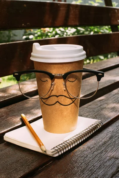 Close up view of coffee to go with eyeglasses, notebook and pencil on wooden bench — Stock Photo