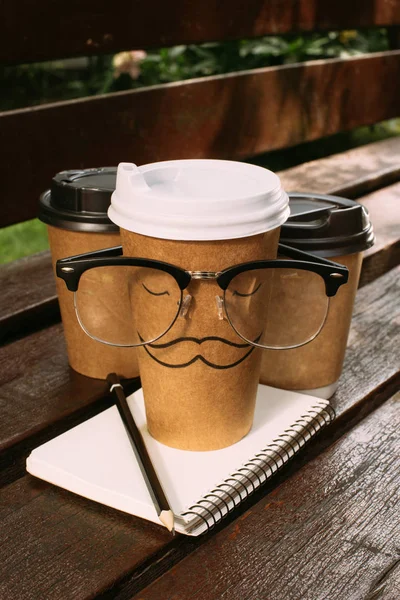 Close up view of coffee to go, eyeglasses and notebook on wooden bench — Stock Photo
