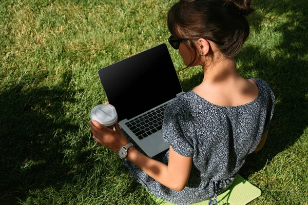 Vista trasera del freelancer con café para ir a trabajar en el ordenador portátil en el césped verde en el parque - foto de stock