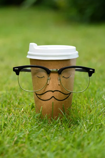 Vista de cerca de la taza desechable con signo de bigote y gafas en el césped verde - foto de stock