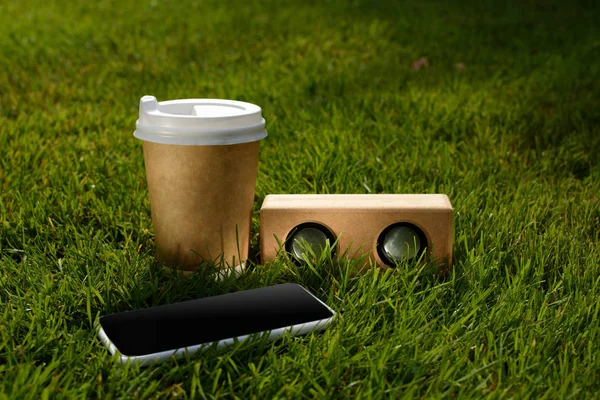 Close up view of coffee to go, smartphone and audio speaker on green grass — Stock Photo