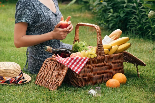 Cropped image of woman sitting on green grass at picnic and holding apple — Stock Photo