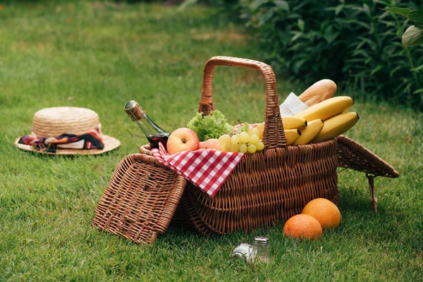 Deliziosi frutti e bottiglia di champagne in cesto di vimini su erba verde al picnic — Foto stock