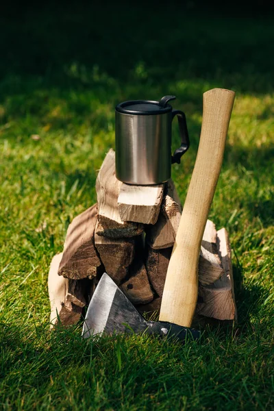 Thermos bouteille sur pile de bois de chauffage sur herbe verte dans le parc — Photo de stock