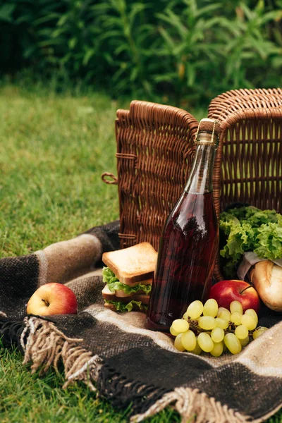 Volteado cesta con frutas y botella de champán en la manta en el parque - foto de stock