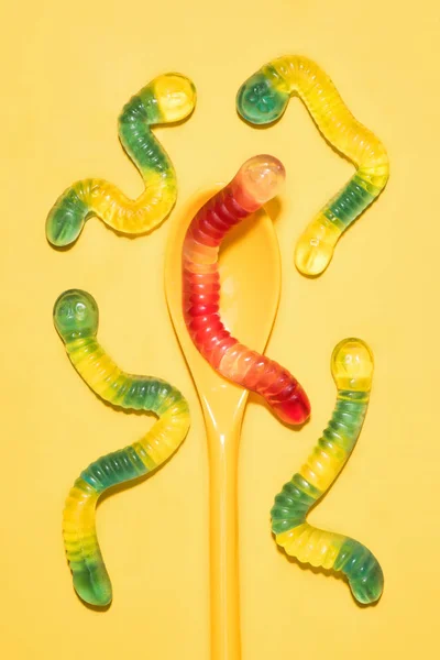 Top view of colorful gummy worms with spoon on yellow — Stock Photo