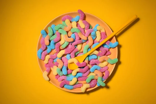 Gummiwürmer mit Löffel auf Teller und auf gelb — Stockfoto