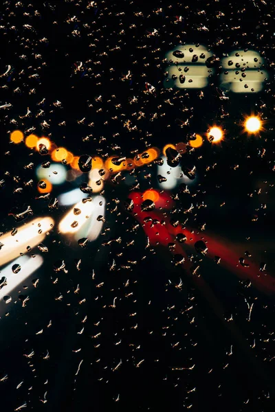 Vue rapprochée des gouttes de pluie sur la fenêtre et des lumières de la ville bokeh en arrière-plan — Photo de stock