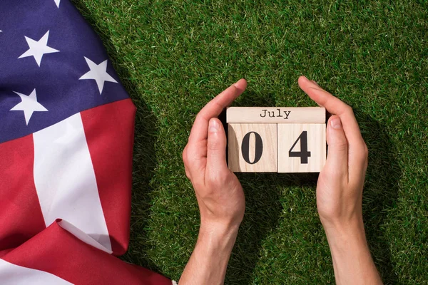 Tiro recortado de homem segurando calendário com data de 4 de julho com bandeira americana na grama verde, conceito de dia de independência das américas — Fotografia de Stock