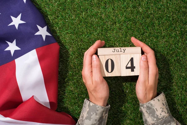 Colpo ritagliato di soldato in uniforme militare in possesso di calendario con 4 luglio data con bandiera americana su erba verde, concetto di indipendenza americana giorno — Foto stock