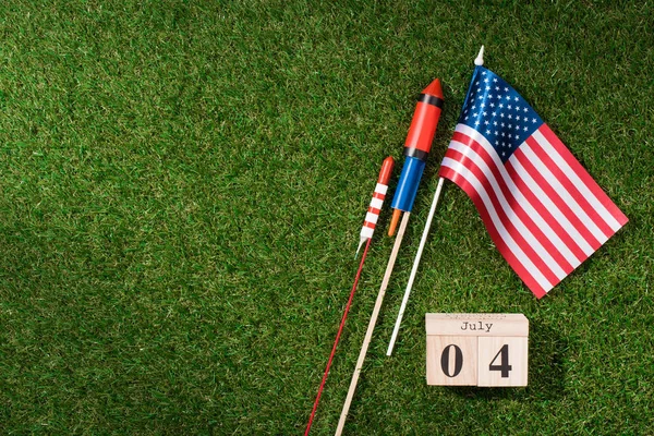 Flat lay com bandeira americana, calendário de madeira com data de 4 de julho e fogos de artifício na grama verde, conceito de dia da independência das américas — Fotografia de Stock