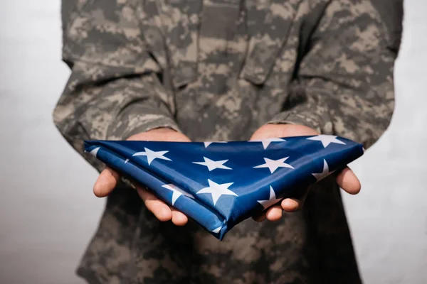 Partial view of soldier in military uniform showing folded flag in hands, americas independence day concept — Stock Photo