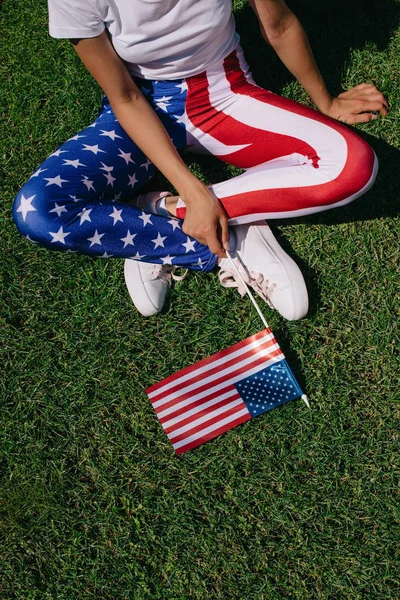 Partial view of woman with flagpole in leggins with american flag pattern resting on green lawn, americas independence day holiday concept — Stock Photo