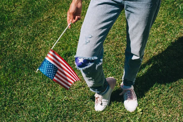 Cropped shot of woman in denim with american flagpole in hand standing on green grass, 4th july holiday concept — Stock Photo