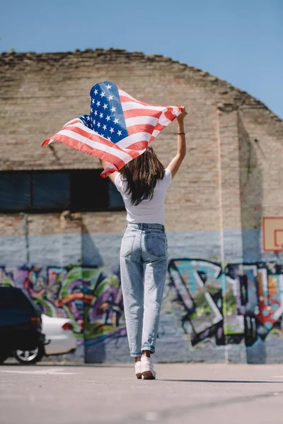 Back view of woman with american flag in hands standing on street, 4th july holiday concept — Stock Photo