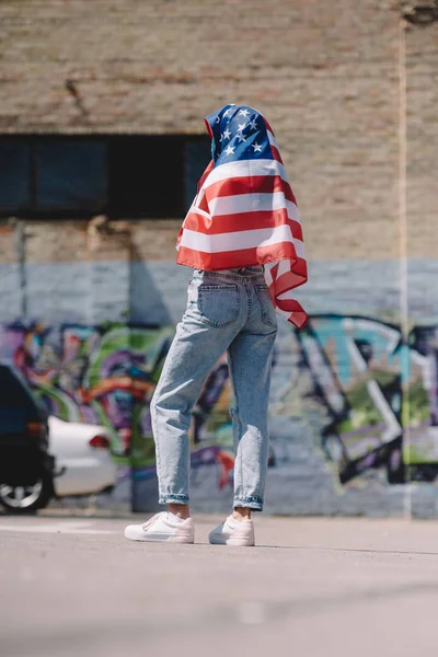 Visão traseira da mulher com bandeira americana em mãos de pé na rua, conceito de férias de 4 de julho — Fotografia de Stock