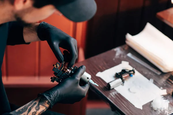 Enfoque selectivo del artista del tatuaje en guantes con máquina de tatuaje en el salón - foto de stock