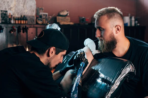 Side view of tattoo artist in gloves working on tattoo on shoulder in salon — Stock Photo