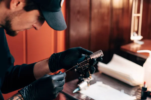 Selective focus of tattoo artist in gloves with tattooing machine in salon — Stock Photo