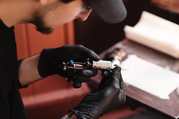 Selective focus of tattoo artist in gloves with tattooing machine in salon — Stock Photo