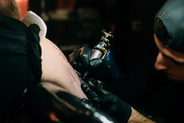 Enfoque selectivo del artista del tatuaje en guantes con máquina de tatuaje trabajando en el tatuaje en el hombro en el salón - foto de stock
