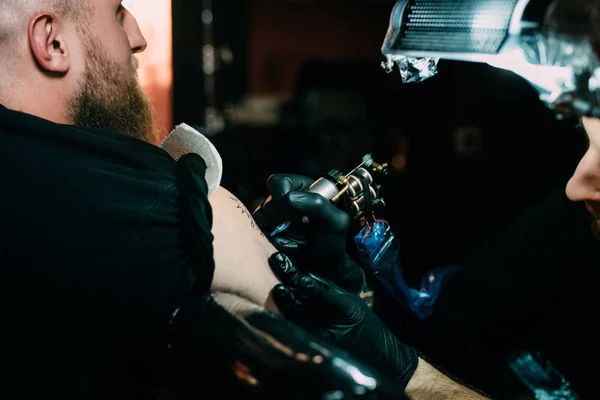 Selektiver Fokus des Tätowierers in Handschuhen mit Tätowiermaschine, die im Salon an der Tätowierung auf der Schulter arbeitet — Stockfoto