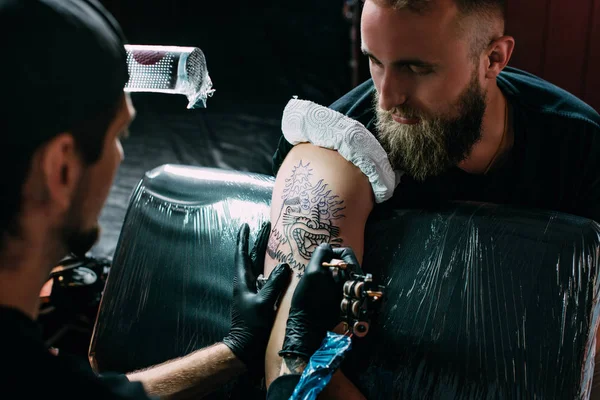 Вибірковий фокус художника татуювання в рукавичках з татуювальною машиною, що працює на татуюванні на плечі в салоні — стокове фото