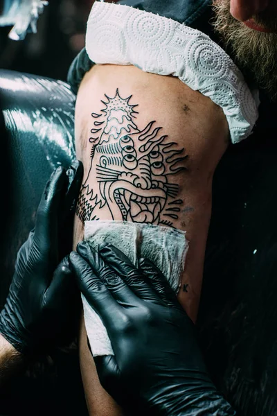 Vista parcial del artista del tatuaje en guantes trabajando en tatuaje en el hombro en el salón - foto de stock