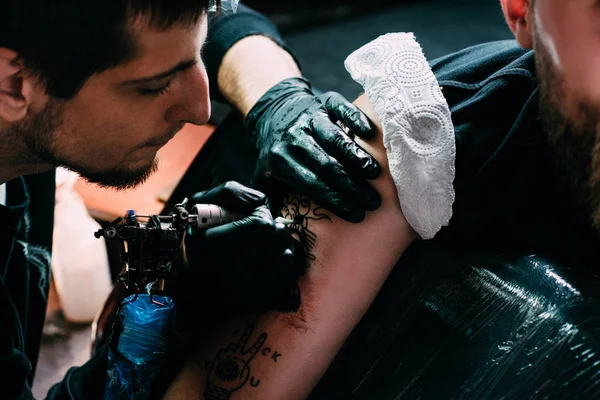 Cropped shot of focused tattoo artist in gloves working on tattoo on shoulder in salon — Stock Photo