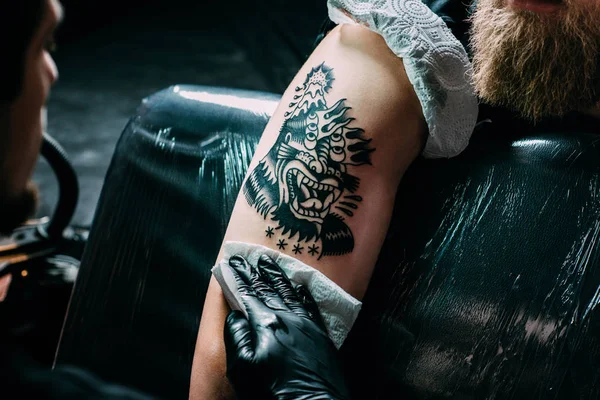 Частковий вид художника татуювання в рукавичках, що працюють на татуюванні на плечі в салоні — стокове фото