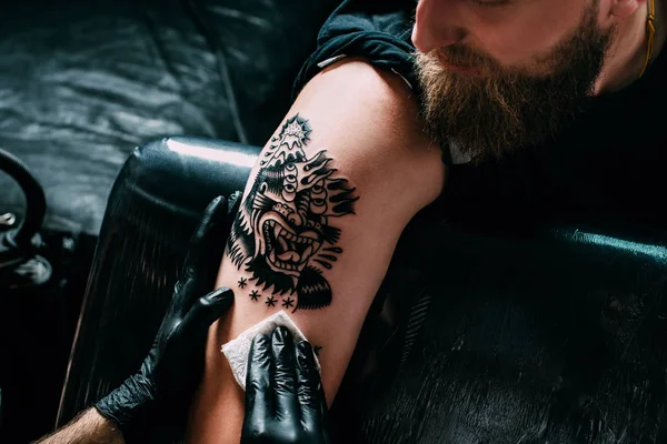 Обрезанный снимок татуировщика в перчатках, работающего на татуировке на плече в салоне — стоковое фото