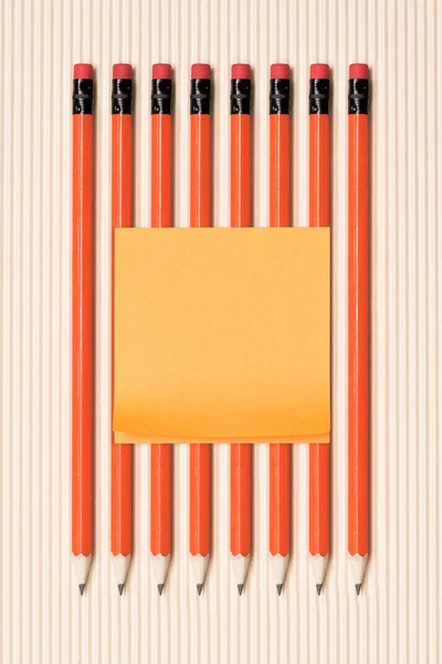 Top view of empty stick it note on graphite pencils with erasers placed in row on beige — Stock Photo