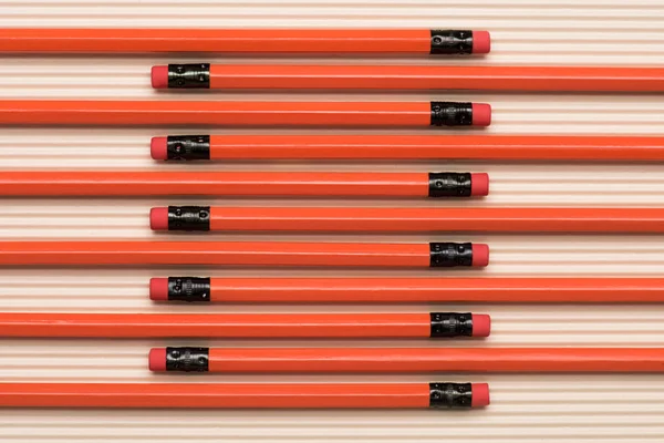 Vista desde arriba de lápices de grafito rojo con gomas de borrar colocadas en fila sobre beige - foto de stock